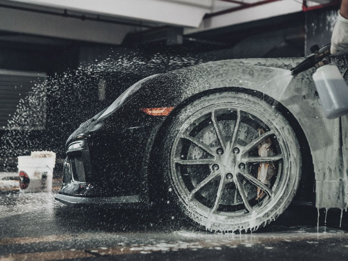 Snow foam being rinsed off a black sports car in the bay