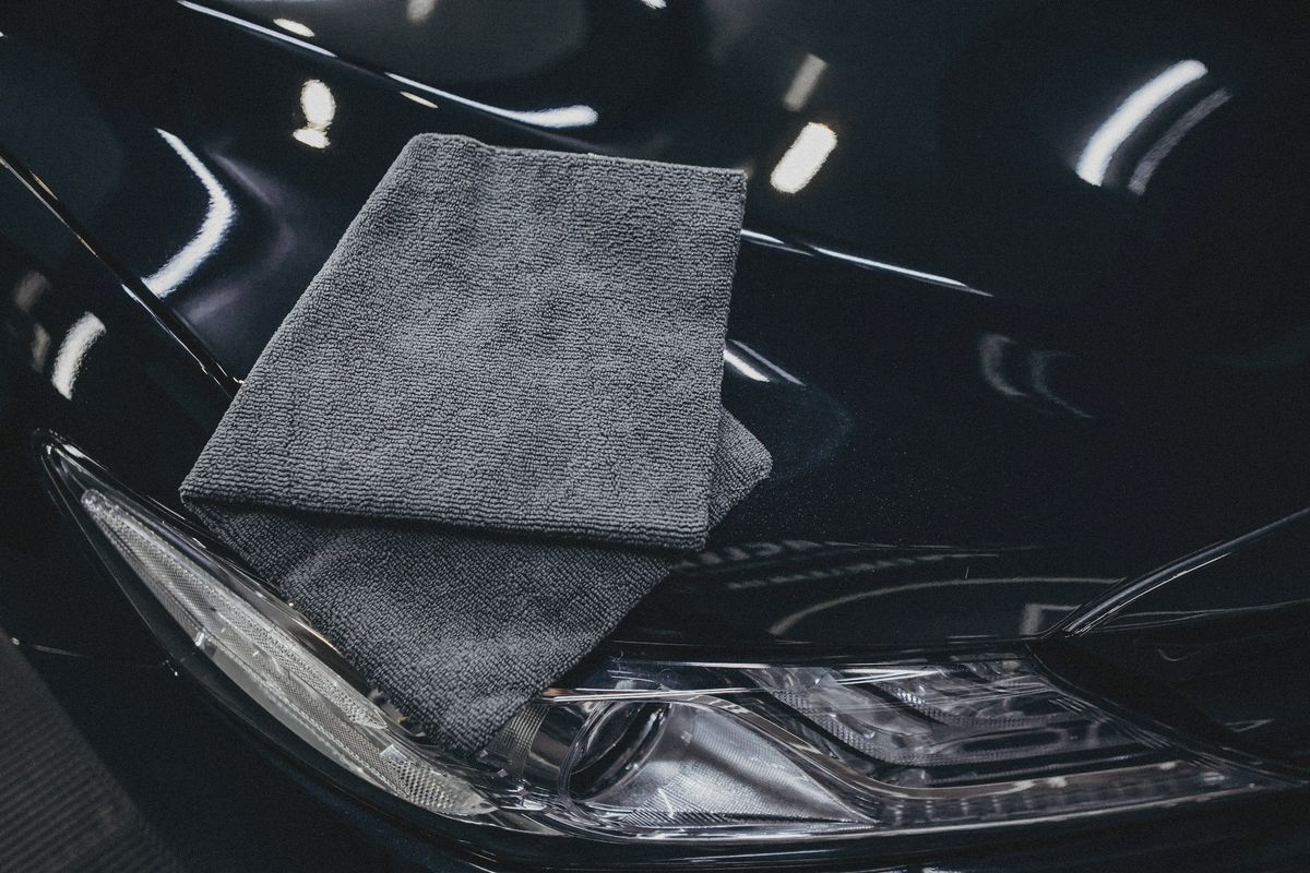 A grey microfibre towel resting on the freshly coated bonnet of a black car