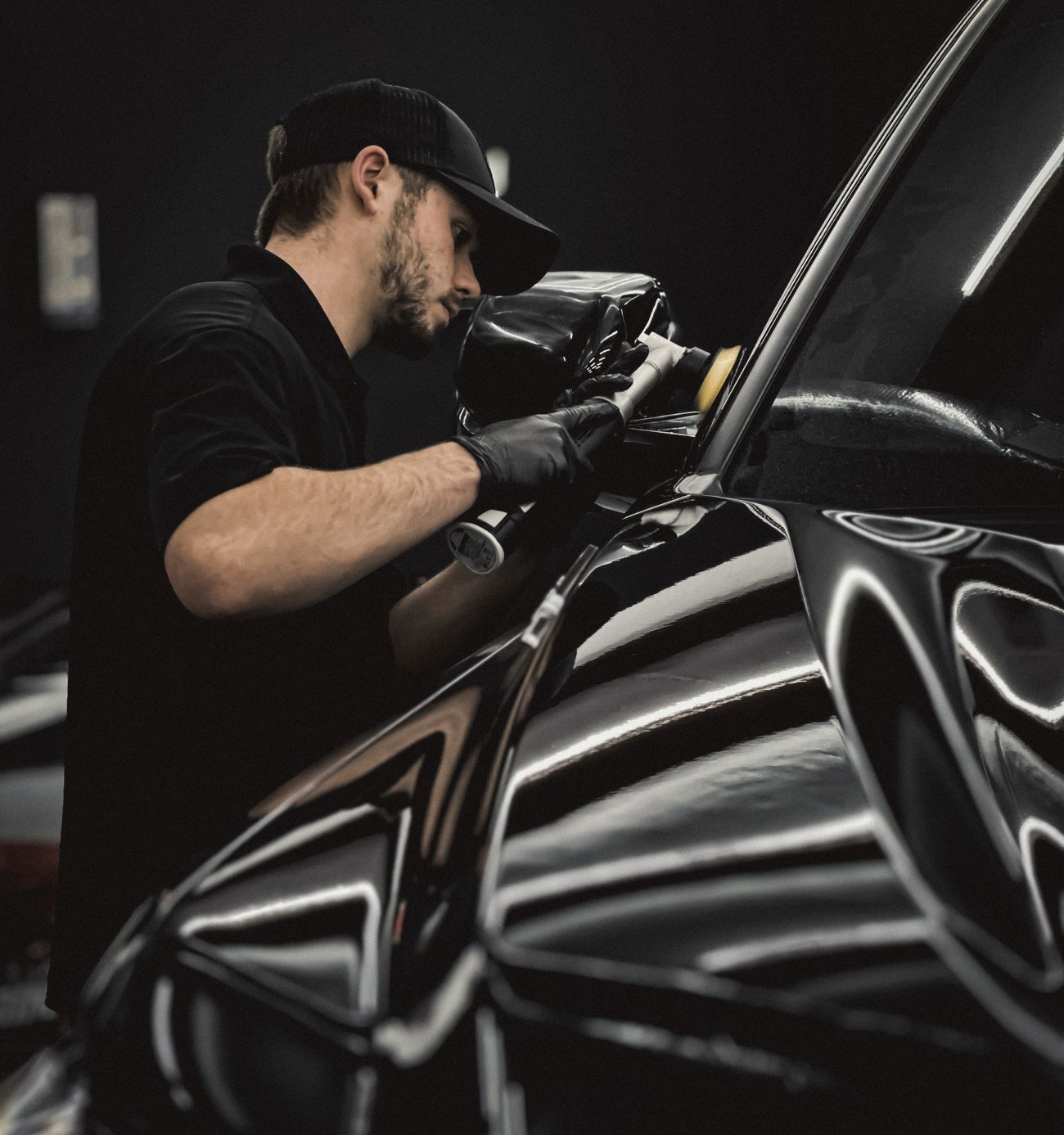 A detailer in black gloves inspecting the reflection in a freshly corrected black door