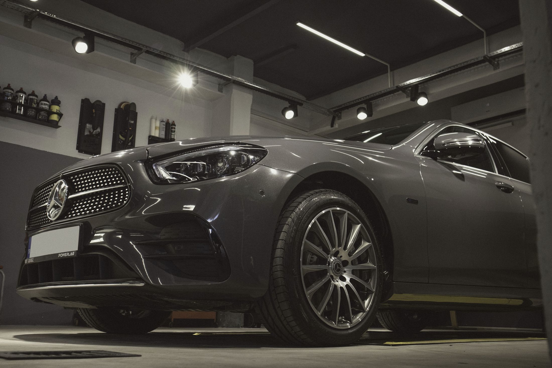 A dark grey sedan under track lights in the Raking Light bay, products on the wall behind